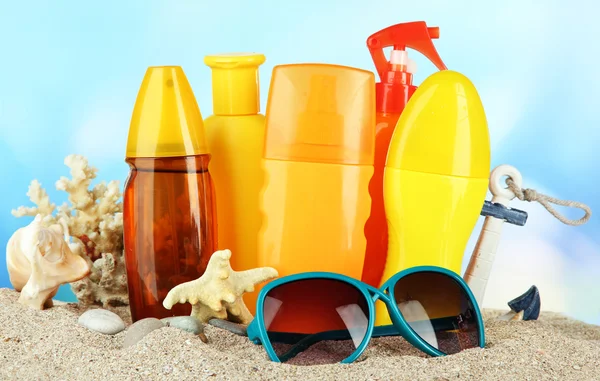 Botellas con crema bronceadora y gafas de sol, sobre fondo azul — Foto de Stock