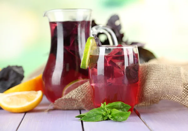 Limonada de manjericão vermelho em jarro e vidro, na mesa de madeira, no fundo brilhante — Fotografia de Stock