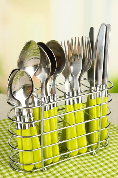 Knives, forks and spoons in metal stand on table on bright background — Stock Photo, Image