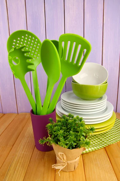 Plastic kitchen utensils in stand with clean dishes on table on wooden background — Stock Photo, Image