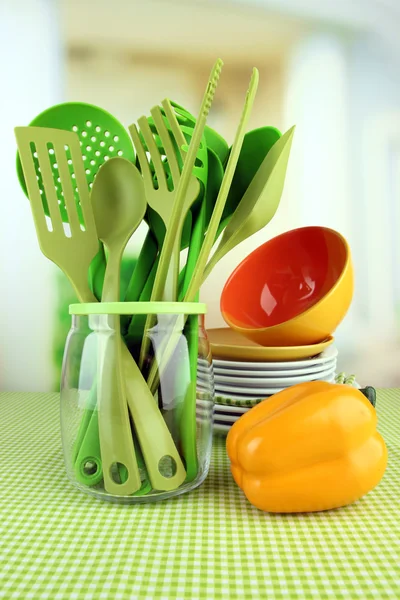 Пластикове кухонне начиння в підставці з чистим посудом на скатертині на яскравому фоні — стокове фото