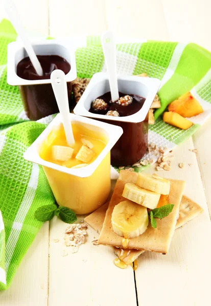 Sobremesas de creme saborosas com pedaços de frutas frescas, biscoitos e flocos, na cor de fundo de madeira — Fotografia de Stock