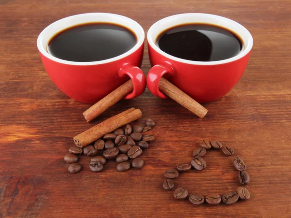 Tazze rosse di caffè forte e chicchi di caffè su sfondo di legno — Foto Stock