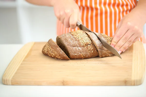 Mujer rebanando pan con semillas de sésamo en la tabla de cortar, de cerca — Foto de Stock