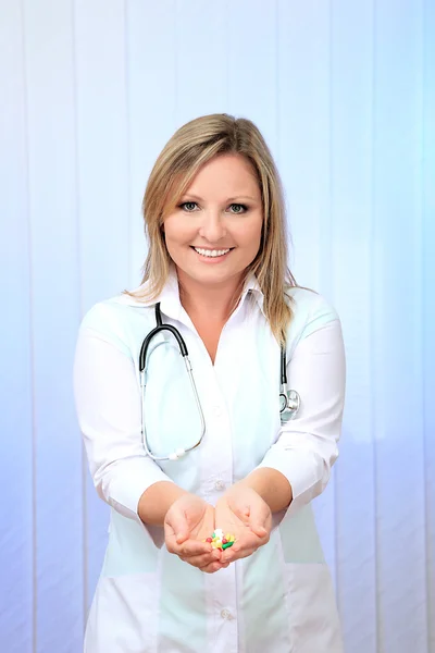 Young beautiful doctor with stethoscope holding multicolor pills, on light background — Stock Photo, Image