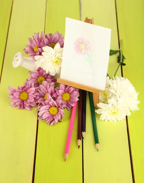 Composition of flowers and small easel with picture on wooden table close-up — Stock Photo, Image