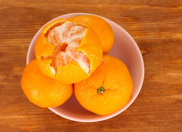 Smakelijke mandarijnen in kleur kom op houten achtergrond — Stockfoto