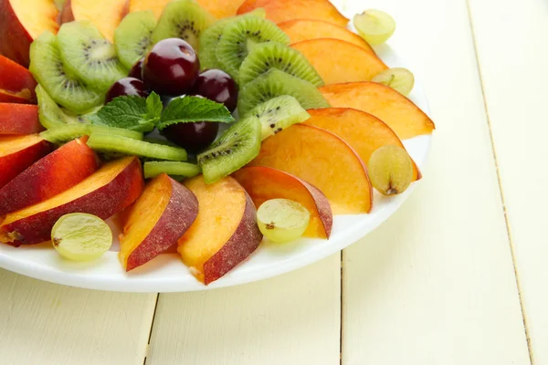 Assortment of sliced fruits on plate, on white wooden table — Stock Photo, Image