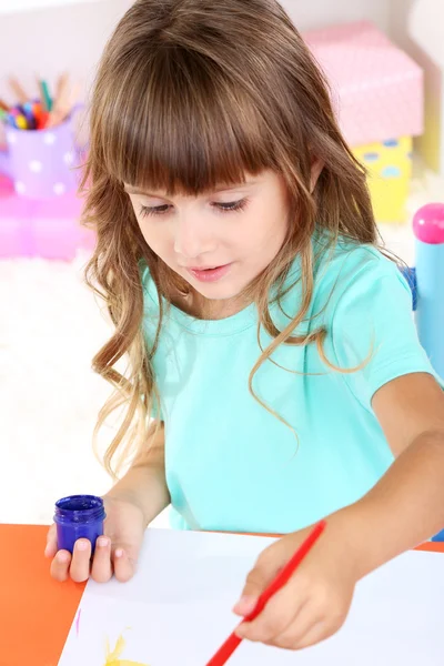 Menina desenha sentado à mesa no quarto em prateleiras fundo — Fotografia de Stock