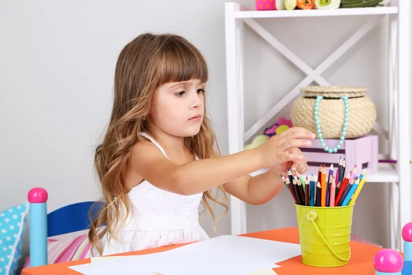 Menina desenha sentado à mesa no quarto no fundo da parede cinza — Fotografia de Stock