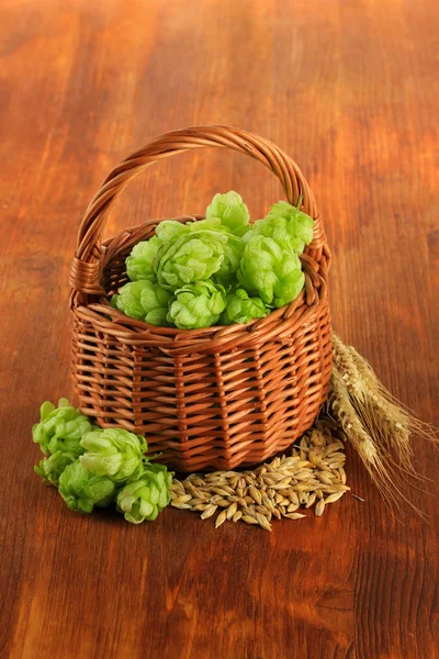 Verse groene hop in rieten mand en gerst, op houten achtergrond — Stockfoto