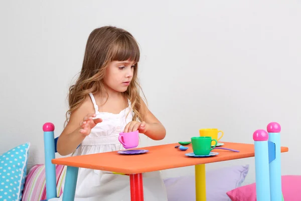 Liten flicka ritar sittande vid bord i rummet på grå vägg bakgrund — Stockfoto