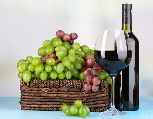成熟的绿色和紫色葡萄与葡萄酒在明亮的背景上的木桌上的篮子里 — 图库照片