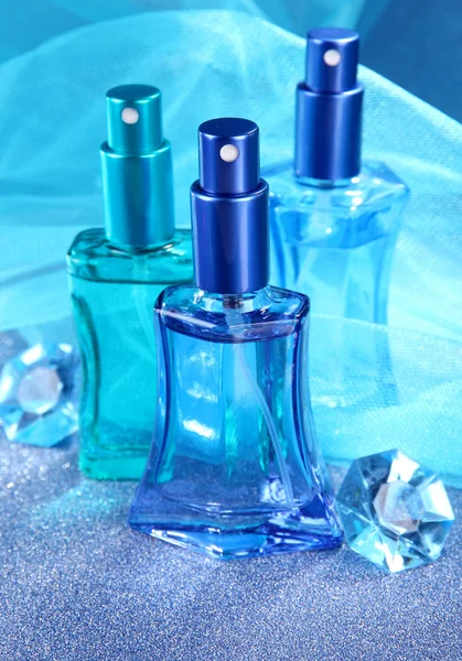 Perfume de mujer en hermosas botellas sobre fondo azul — Foto de Stock