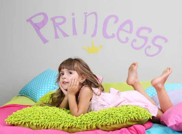 Little girl lying on bed in room on grey wall background — Stock Photo, Image