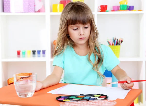 Menina desenha sentado à mesa no quarto em prateleiras fundo — Fotografia de Stock