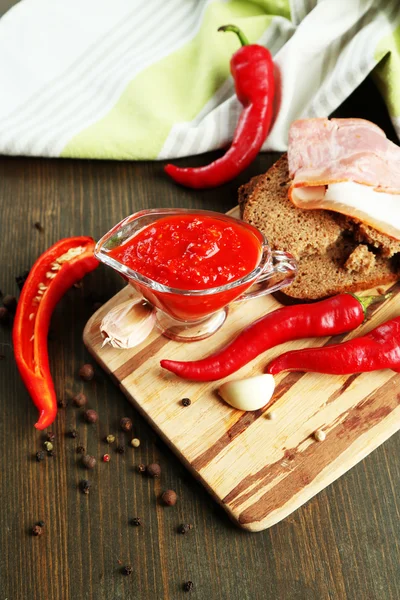 Composition with salsa sauce on bread,, red hot chili peppers and garlic, on napkin, on wooden background — Stock Photo, Image