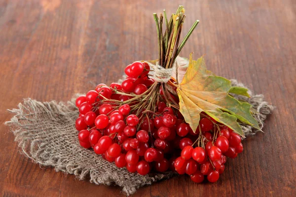 Red berries of viburnum on sackcloth napkin, on wooden background — Stock Photo, Image