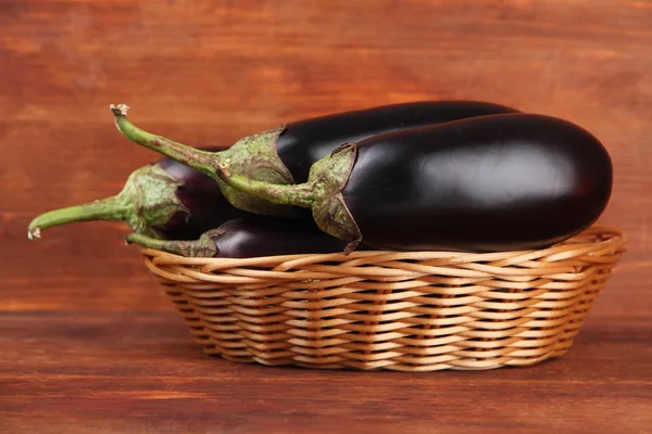 Fresh eggplants in wicker basket on table on wooden background — Stock Photo, Image