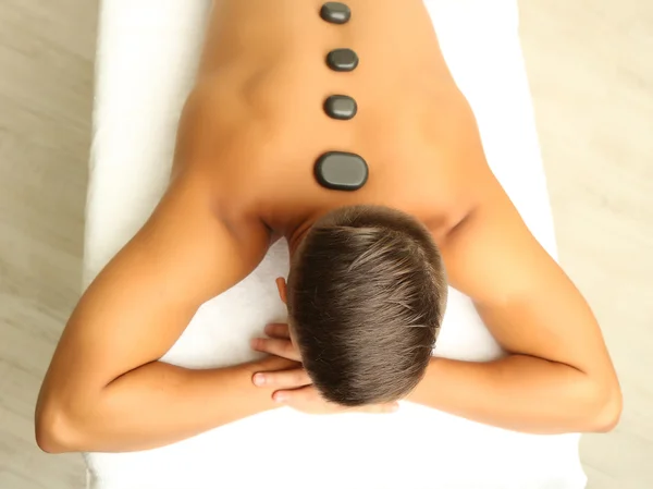 Young man relaxing with hot stones on back before massage — Stock Photo, Image