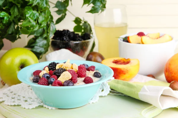 Oatmeal in plate with berries on napkins on wooden board on table on bright background — Stock Photo, Image