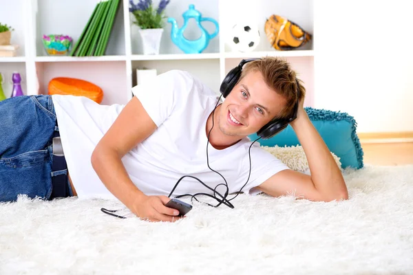 Junger Mann entspannt sich auf Teppich und hört Musik — Stockfoto