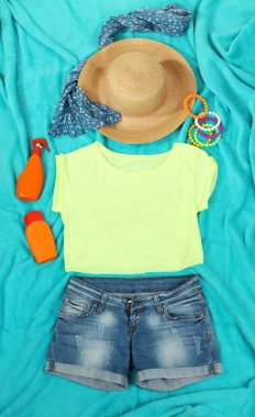Top, shorts and beach items on bright blue background