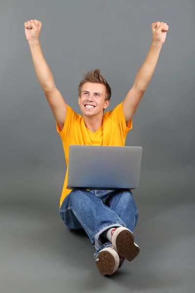 Un joven guapo con portátil sobre fondo gris — Foto de Stock