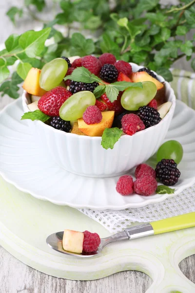 Ensalada de frutas en tazón, sobre mesa de madera, sobre fondo brillante —  Fotos de Stock