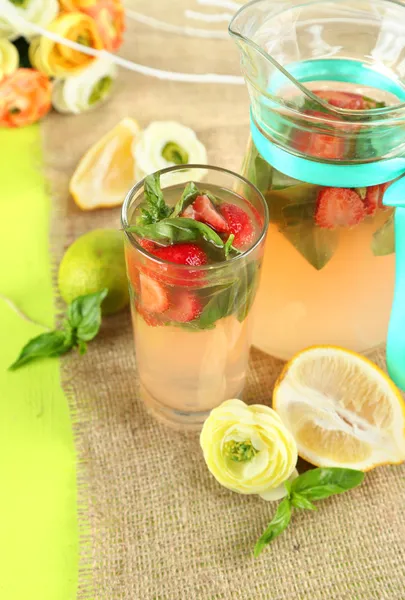 Basil lemonade with strawberry in jug and glass, on wooden table, on bright background — Stock Photo, Image