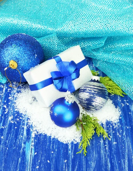 Composition with Christmas balls, gift box and snow on color wooden background — Stock Photo, Image