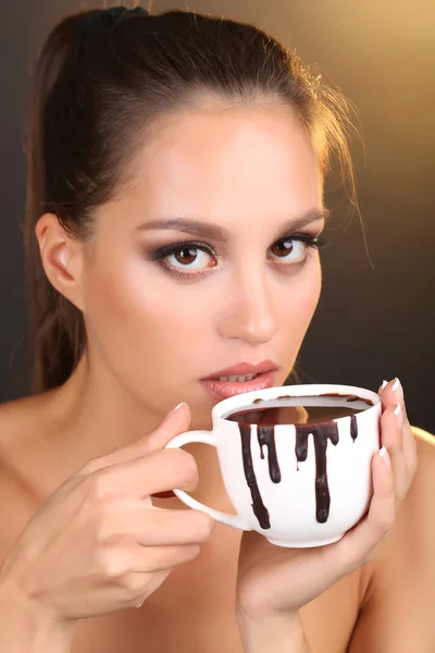 Portrait of beautiful young girl with cup of hot chocolate on brown background — Stock Photo, Image