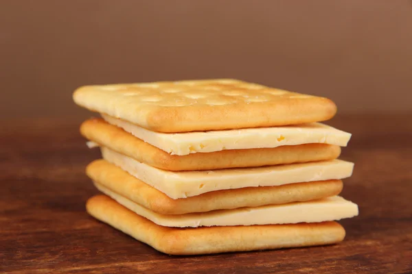 Pyszne krakersy z serem na drewnianym stole na brązowym tle — Zdjęcie stockowe