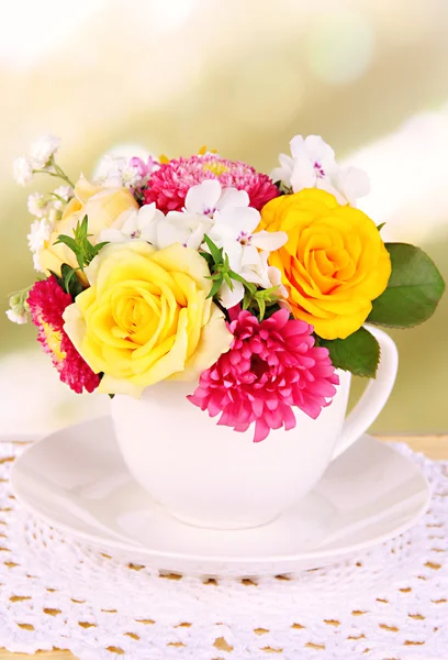 Hermoso ramo de flores brillantes en taza de color, sobre mesa de madera, sobre fondo brillante —  Fotos de Stock