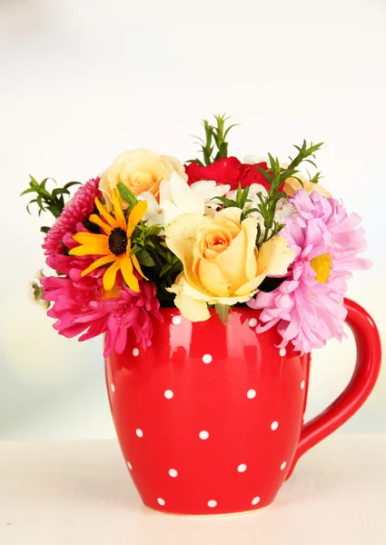 Красивый букет ярких цветов в цветной кружке, на деревянном столе, на светлом фоне — стоковое фото