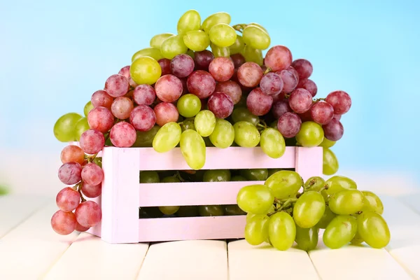 Ripe green and purple grapes in wooden box on wooden table on natural background — Stock Photo, Image