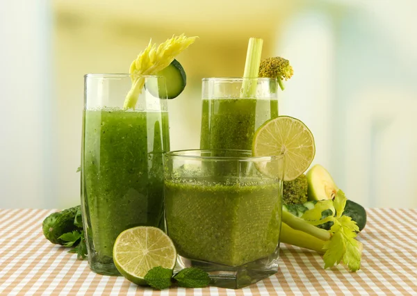 Vasos de jugo de verduras verdes y verduras sobre mantel sobre fondo brillante — Foto de Stock