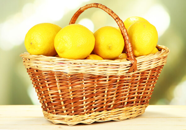 Ripe lemons in wicker basket on table on bright background