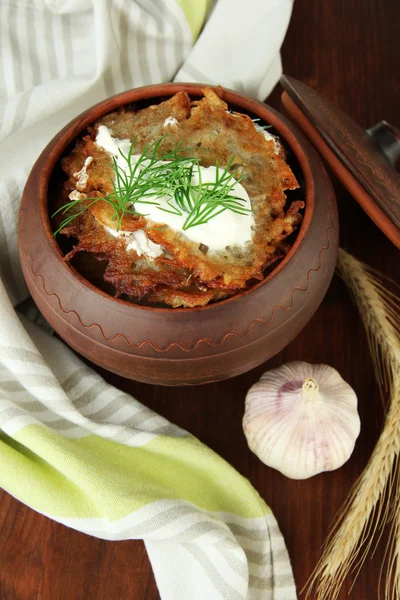 Potato pancakes in pot, on wooden background — Stock Photo, Image