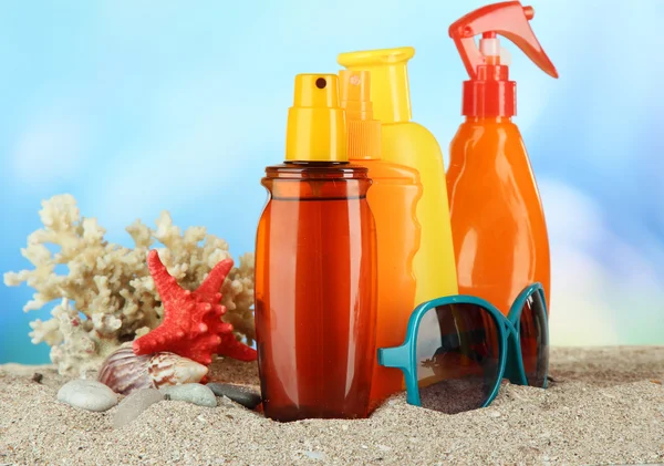 Garrafas com creme bronzeado e óculos de sol, sobre fundo azul — Fotografia de Stock