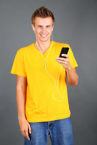 Schöner junger Mann hört Musik auf grauem Hintergrund — Stockfoto