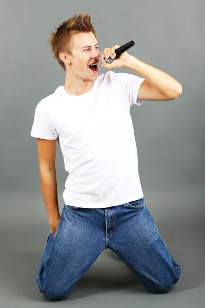 Bonito jovem canta em fundo cinza — Fotografia de Stock