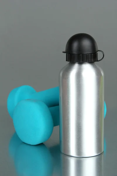 Sportflasche und Hanteln auf grauem Hintergrund — Stockfoto