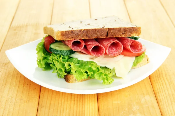 Matig smörgås med salami korv och grönsaker på vit platta, på trä bakgrund — Stockfoto