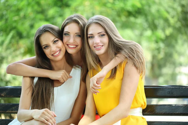 Three beautiful young woman sitting on bench in summer park — Stock Photo, Image