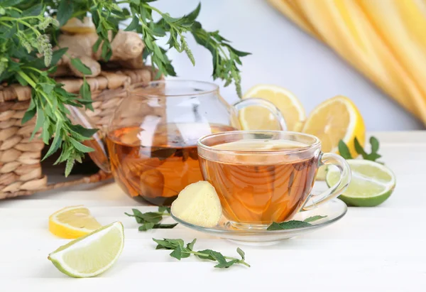 Hervidor de agua y taza de té con jengibre en la mesa de madera sobre fondo brillante —  Fotos de Stock