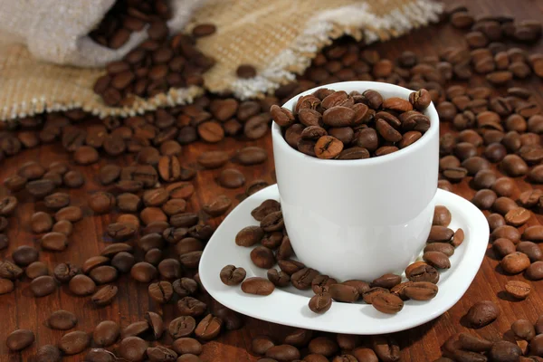 Grãos de café em xícara no fundo de madeira — Fotografia de Stock