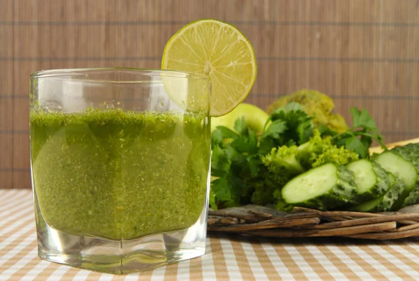 Gelas jus sayuran hijau dan sayuran pada taplak meja pada latar belakang bambu — Stok Foto