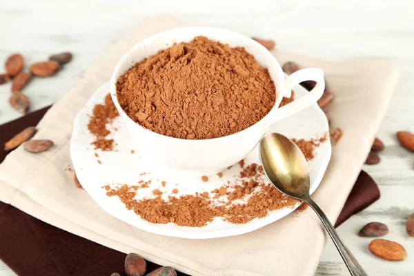 Cocoa powder in cup on napkin on wooden table — Stock Photo, Image