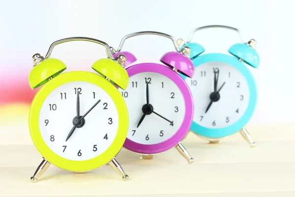 Coloridos relojes de alarma en la mesa sobre fondo claro — Foto de Stock